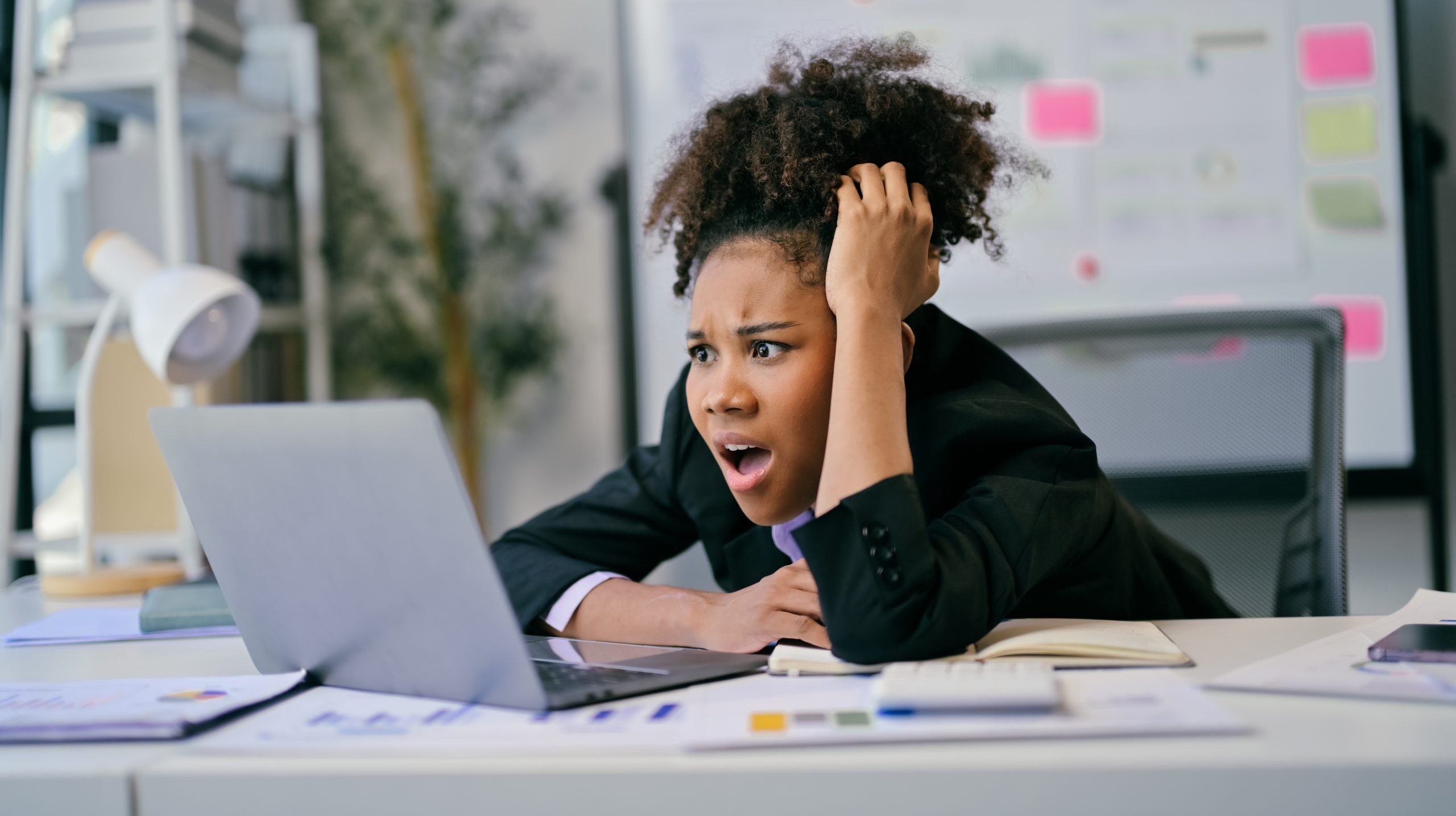 Shocked businesswoman looking at laptop with worried expression in office